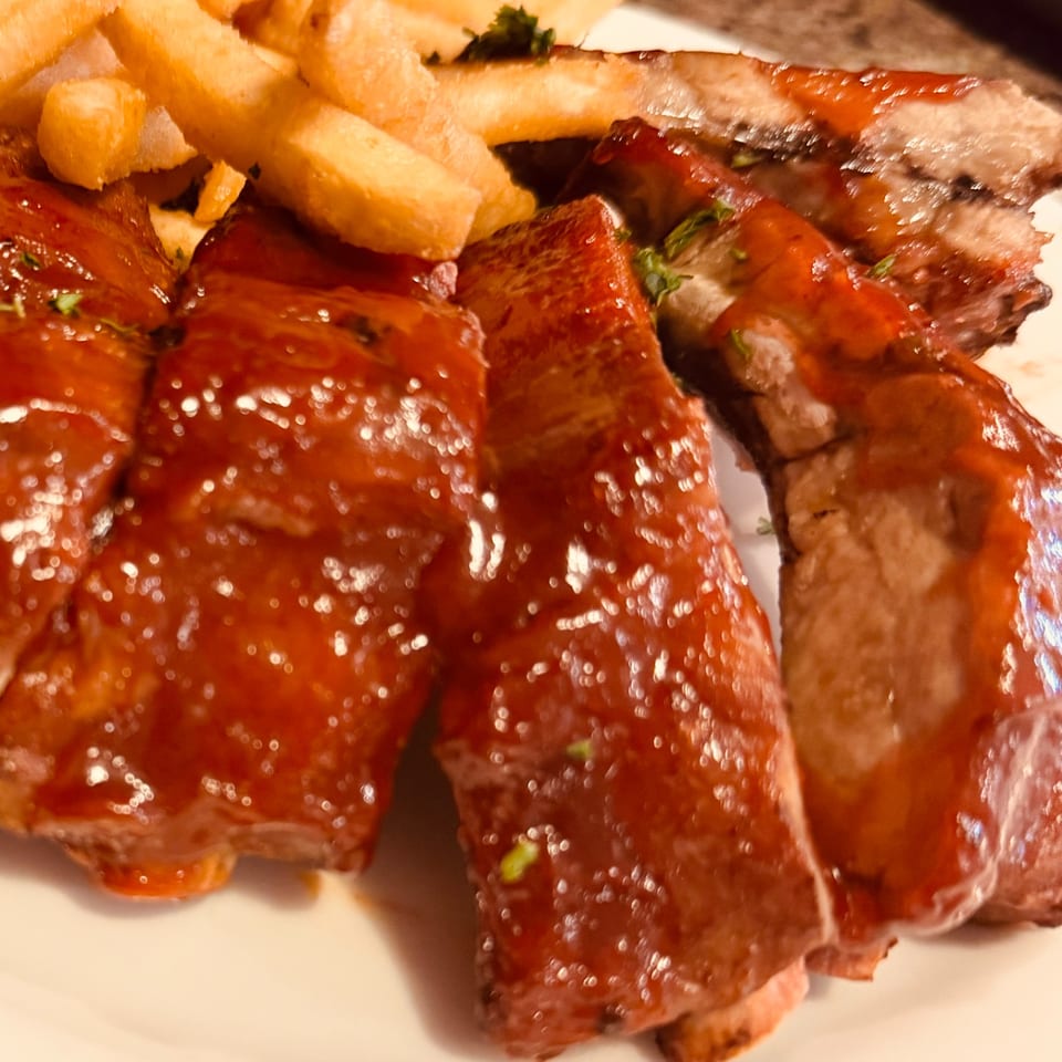 Close-up of Corner Post Diner's BBQ ribs with shiny sauce and a side of golden french fries.