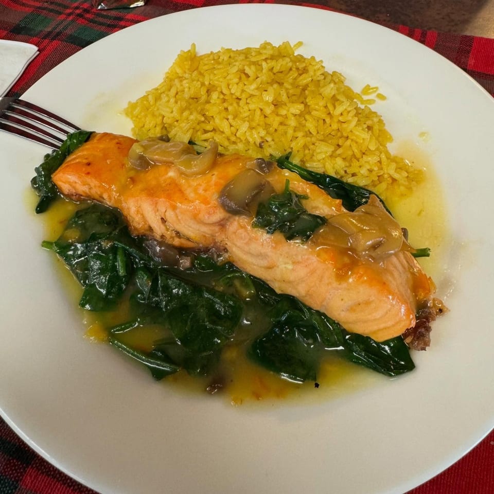 Salmon fillet with mushroom sauce, spinach, and yellow rice on a white plate at Corner Post Diner.